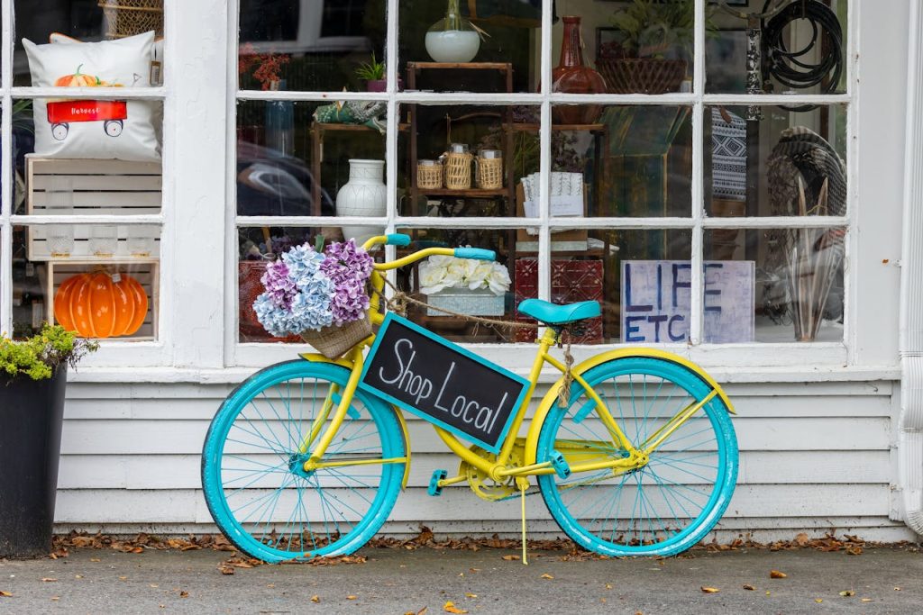 A colorful bicycle with flowers and Shop Local sign outside a store in Sudbury, MA.
